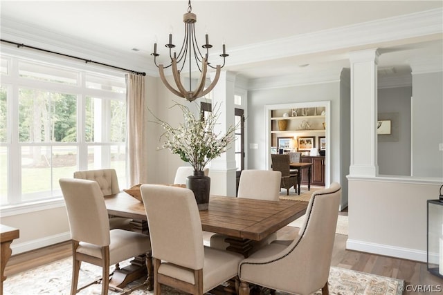 dining space featuring light wood-type flooring, a chandelier, built in shelves, ornamental molding, and ornate columns