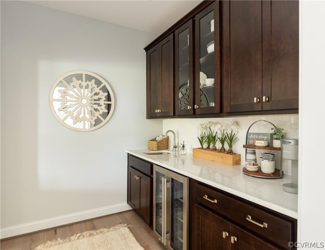 bar featuring beverage cooler, sink, dark brown cabinets, and light hardwood / wood-style floors