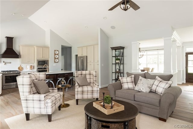 living room featuring high vaulted ceiling, ceiling fan with notable chandelier, and light wood-type flooring