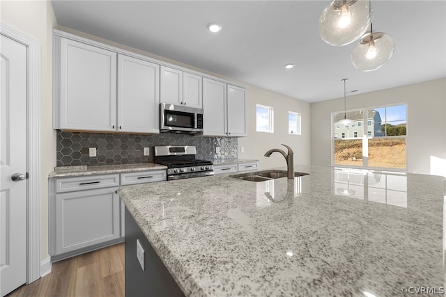 kitchen with pendant lighting, sink, stainless steel appliances, light stone counters, and white cabinets