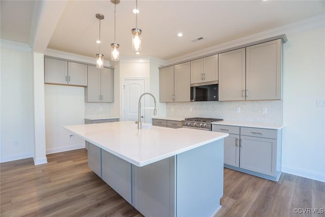 kitchen with stainless steel appliances, ornamental molding, a kitchen island with sink, and decorative light fixtures