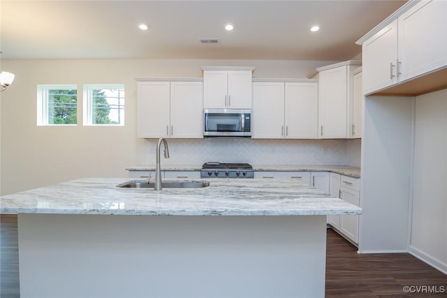 kitchen with white cabinetry, sink, range, light stone countertops, and a center island with sink