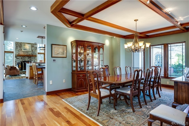 dining room featuring a stone fireplace, coffered ceiling, a notable chandelier, light hardwood / wood-style floors, and beam ceiling