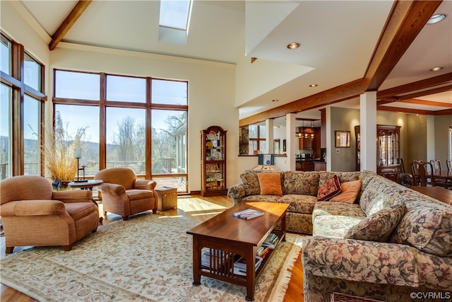 living room with beam ceiling, a skylight, a high ceiling, and light wood-type flooring