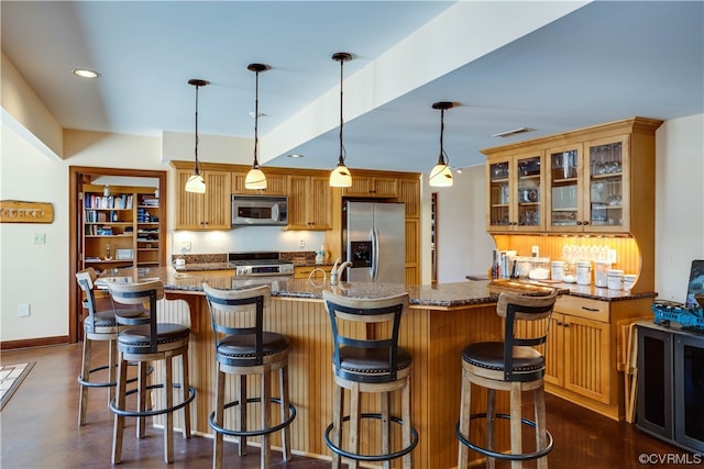 kitchen featuring a breakfast bar, appliances with stainless steel finishes, hanging light fixtures, an island with sink, and dark stone counters