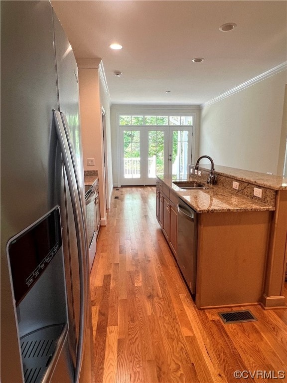 kitchen with appliances with stainless steel finishes, sink, light wood-type flooring, light stone countertops, and ornamental molding