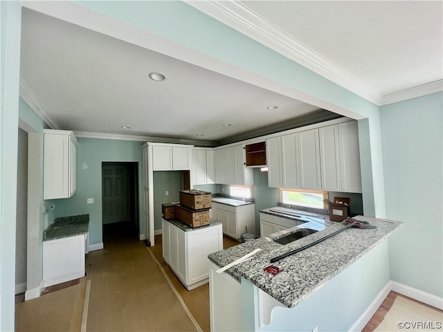 kitchen with a sink, light wood-style floors, a peninsula, crown molding, and baseboards