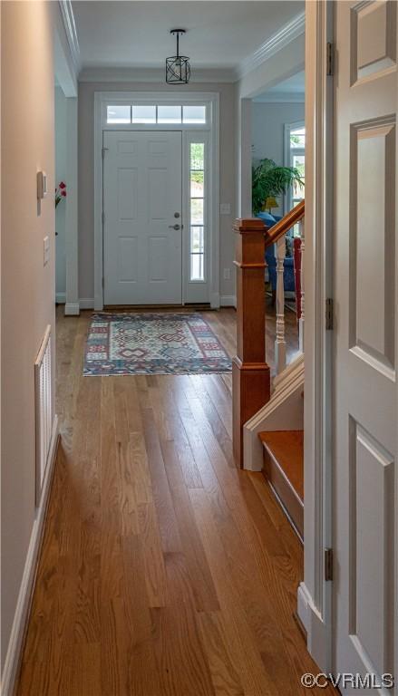 foyer with visible vents, wood finished floors, crown molding, baseboards, and stairs