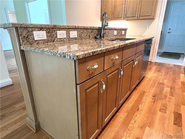 kitchen with baseboards, light stone countertops, an island with sink, light wood-style flooring, and a sink