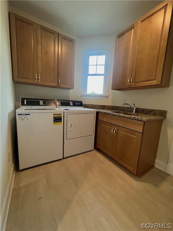 washroom with washing machine and clothes dryer, baseboards, light wood-style flooring, cabinet space, and a sink