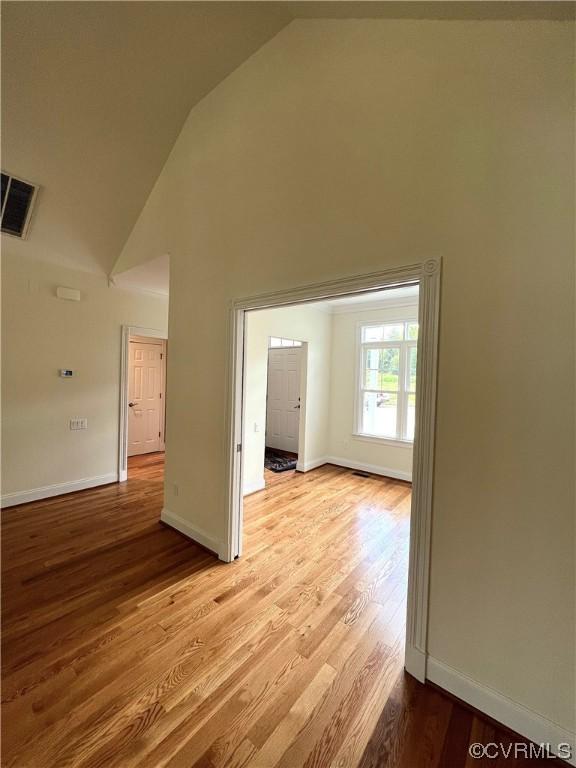 empty room featuring visible vents, light wood-style floors, baseboards, and high vaulted ceiling