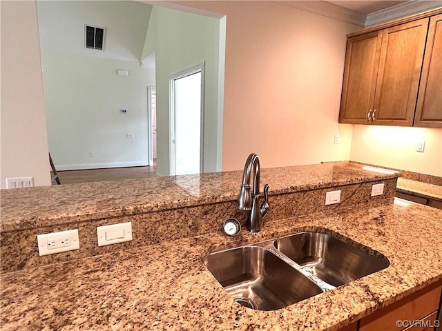 kitchen featuring brown cabinetry, light stone countertops, visible vents, a sink, and crown molding