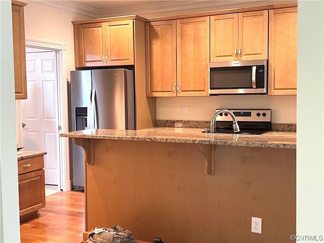 kitchen with light stone countertops, ornamental molding, appliances with stainless steel finishes, a kitchen breakfast bar, and light wood-type flooring