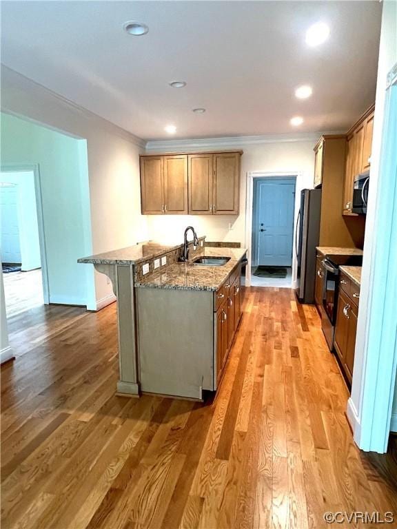 kitchen with light wood-style flooring, a sink, appliances with stainless steel finishes, a breakfast bar area, and light stone countertops