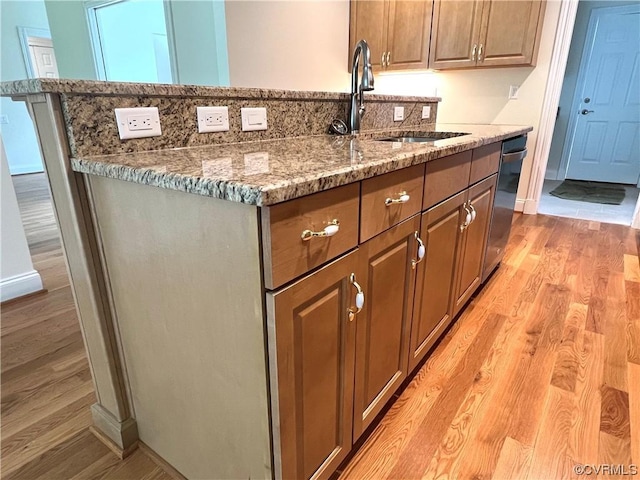 kitchen featuring light stone counters, baseboards, a center island with sink, light wood finished floors, and a sink