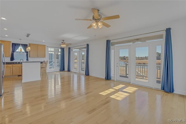 unfurnished living room featuring light wood finished floors, recessed lighting, a sink, and a healthy amount of sunlight