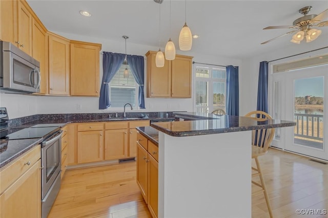 kitchen featuring light brown cabinets, stainless steel appliances, a kitchen island, and a sink