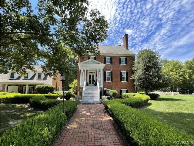 view of front of house with brick siding, a chimney, and a front yard