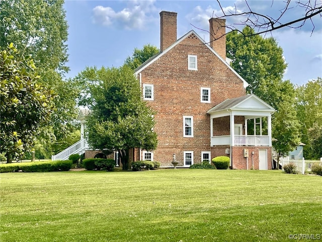 rear view of property with a balcony, a lawn, brick siding, and a chimney