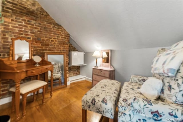 bedroom with vaulted ceiling, brick wall, baseboards, and wood finished floors