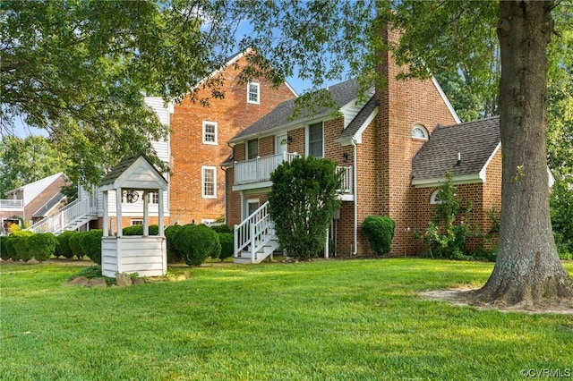 view of front of property featuring stairway, brick siding, a balcony, and a front lawn