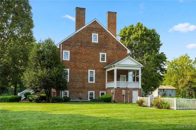 back of house featuring brick siding, fence, a lawn, a chimney, and a balcony