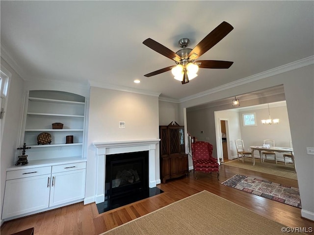 unfurnished living room with built in features, a fireplace with flush hearth, ornamental molding, wood finished floors, and ceiling fan with notable chandelier