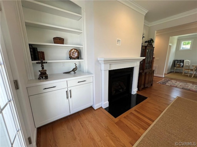 unfurnished living room with a fireplace with flush hearth, baseboards, built in features, light wood finished floors, and crown molding