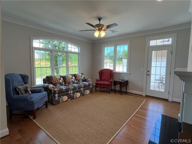 living area with ornamental molding, wood finished floors, a ceiling fan, and baseboards