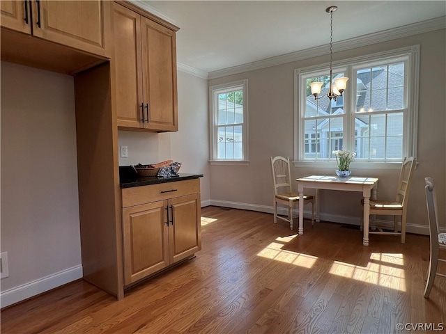 kitchen with a chandelier, baseboards, ornamental molding, light wood-type flooring, and dark countertops