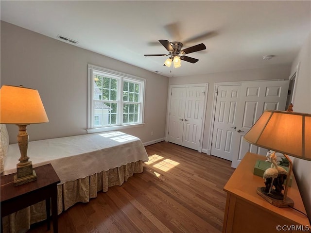 bedroom with wood finished floors, a ceiling fan, visible vents, baseboards, and two closets