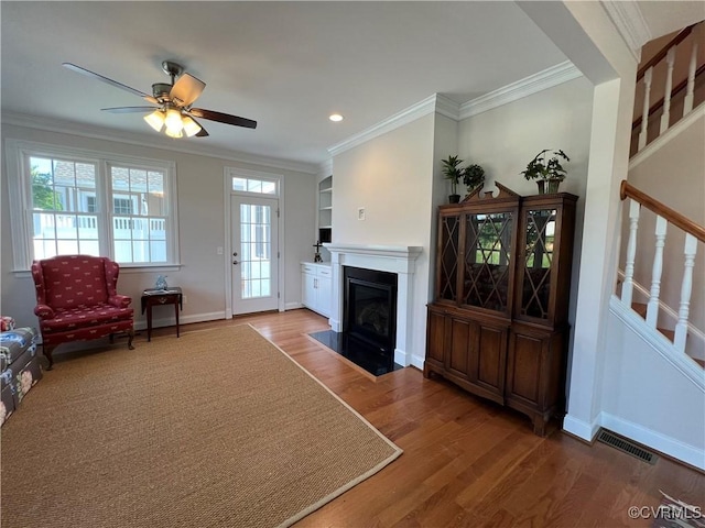 living area featuring baseboards, visible vents, a fireplace with flush hearth, ornamental molding, and wood finished floors