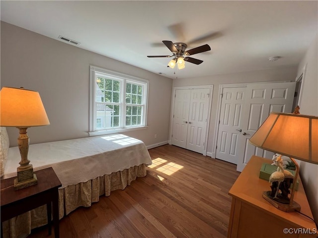 bedroom featuring multiple closets, visible vents, ceiling fan, wood finished floors, and baseboards