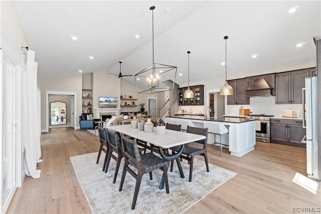 dining space featuring light wood finished floors, high vaulted ceiling, recessed lighting, a fireplace, and stairs