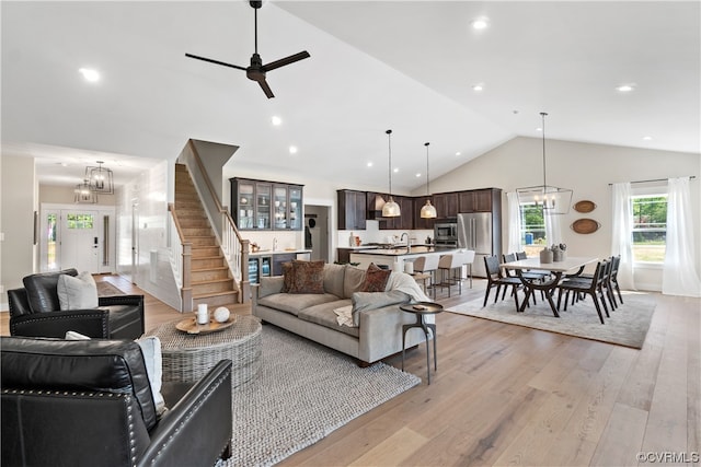 living room with high vaulted ceiling, ceiling fan with notable chandelier, and light wood-type flooring