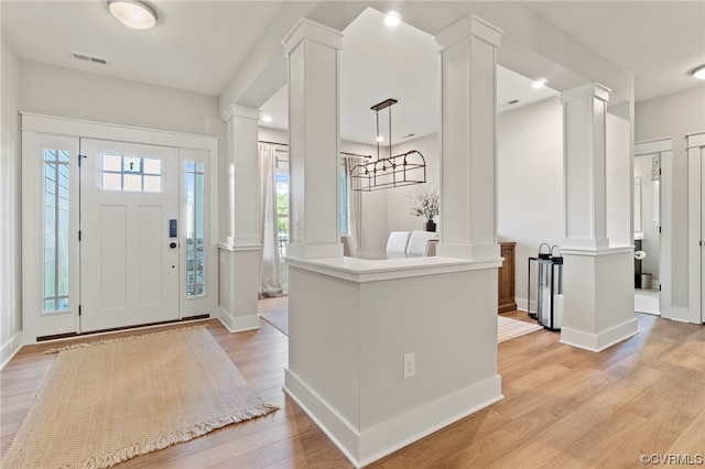 foyer featuring an inviting chandelier, light hardwood / wood-style floors, and decorative columns