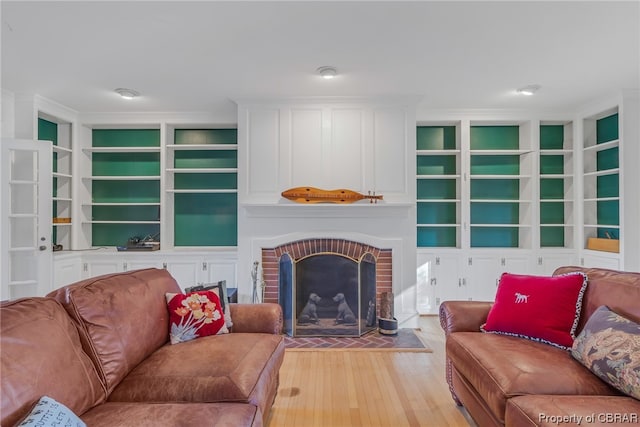 living room featuring built in features, light wood-type flooring, and a fireplace