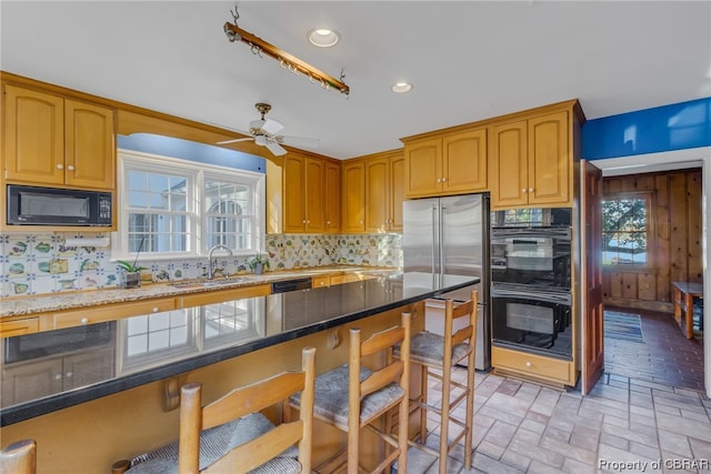 kitchen with ceiling fan, backsplash, dark stone countertops, sink, and black appliances