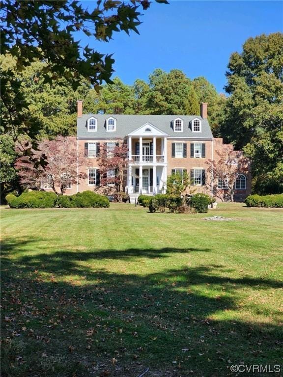 view of front of property with a front yard, a balcony, and a chimney