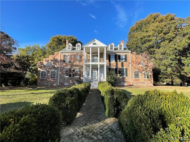 back of house with brick siding, a lawn, a chimney, and a balcony