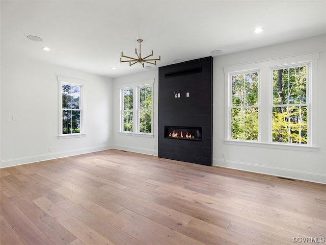 unfurnished living room with light hardwood / wood-style flooring, a tiled fireplace, and a chandelier