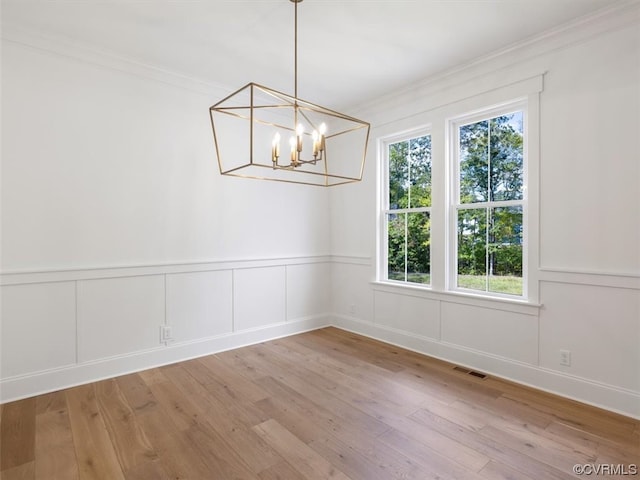 unfurnished dining area with wood-type flooring, ornamental molding, and a chandelier