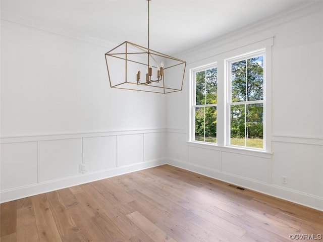 unfurnished dining area featuring a notable chandelier, hardwood / wood-style flooring, and ornamental molding