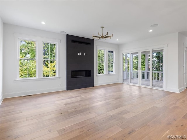 unfurnished living room featuring a tiled fireplace, light hardwood / wood-style floors, and a wealth of natural light