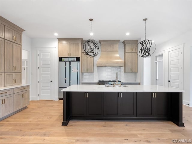 kitchen featuring refrigerator, premium range hood, a center island with sink, and light hardwood / wood-style flooring