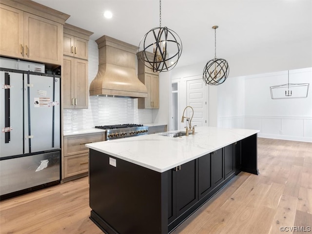 kitchen featuring hanging light fixtures, stainless steel appliances, custom exhaust hood, light hardwood / wood-style flooring, and a kitchen island with sink