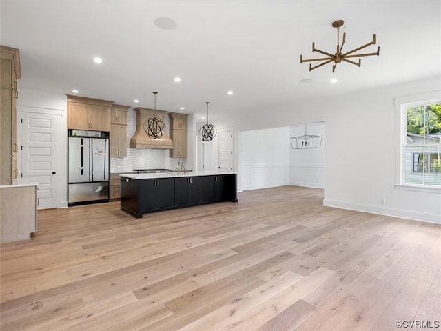 kitchen featuring an island with sink, decorative light fixtures, backsplash, stainless steel appliances, and light wood-type flooring