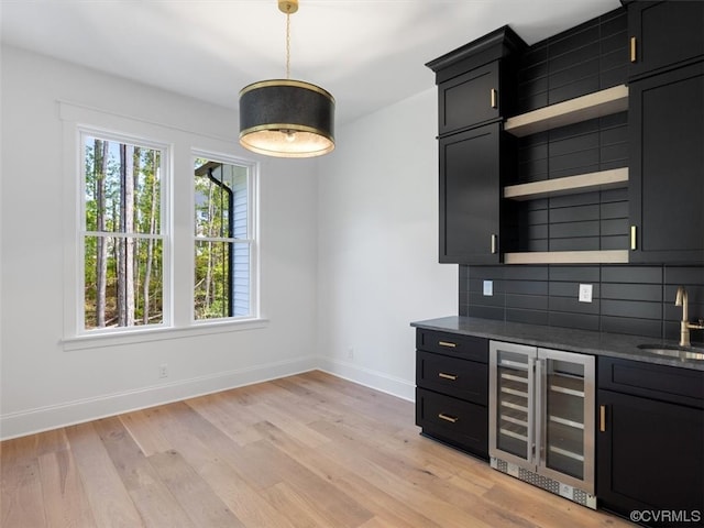 kitchen with light hardwood / wood-style floors, wine cooler, tasteful backsplash, dark stone counters, and sink