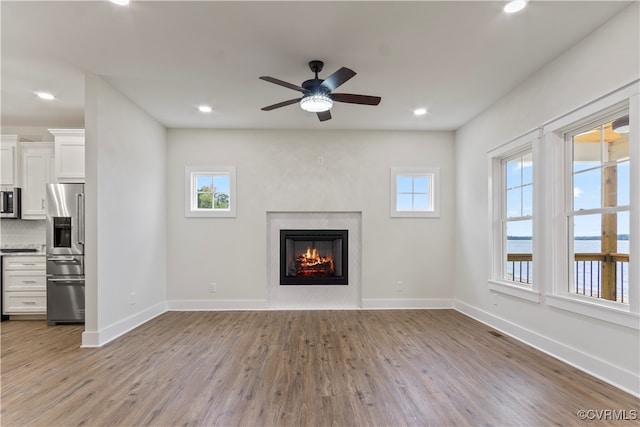 unfurnished living room featuring light hardwood / wood-style flooring, ceiling fan, a fireplace, and a healthy amount of sunlight