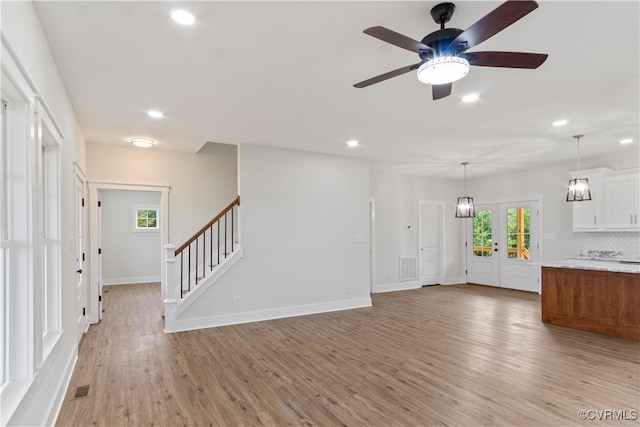 unfurnished living room with ceiling fan with notable chandelier and light hardwood / wood-style floors